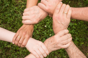 6 Hände, die sich im Kreis jeweils am Handgelenk fassen